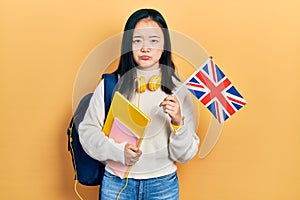 Young chinese girl exchange student holding uk flag depressed and worry for distress, crying angry and afraid