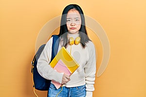 Young chinese girl holding student backpack and books depressed and worry for distress, crying angry and afraid