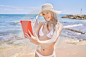 Young chinese girl wearing bikini having video call using touchpad at the beach