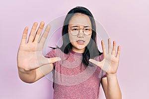 Young chinese girl wearing casual clothes and glasses afraid and terrified with fear expression stop gesture with hands, shouting