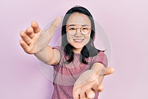 Young chinese girl wearing casual clothes and glasses looking at the camera smiling with open arms for hug