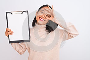 Young chinese inspector woman holding clipboard standing over isolated white background with happy face smiling doing ok sign with