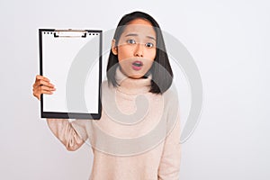 Young chinese inspector woman holding clipboard standing over isolated white background scared in shock with a surprise face,