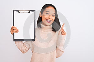 Young chinese inspector woman holding clipboard standing over isolated white background surprised with an idea or question