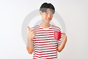 Young chinese man drinking a cup of coffee standing over isolated white background happy with big smile doing ok sign, thumb up