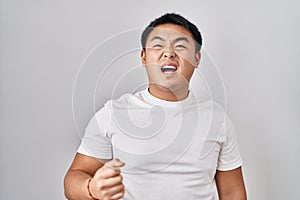 Young chinese man standing over white background angry and mad screaming frustrated and furious, shouting with anger