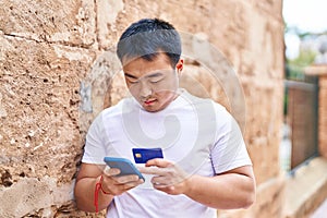 Young chinese man using smartphone and credit card at street