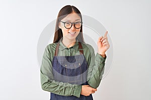 Young chinese shopkeeper woman wearing apron and glasses over isolated white background with a big smile on face, pointing with