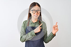 Young chinese shopkeeper woman wearing apron and glasses over isolated white background smiling and looking at the camera pointing