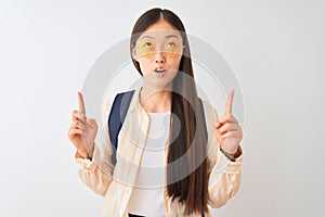 Young chinese student woman wearing glasses and backpack over isolated white background amazed and surprised looking up and