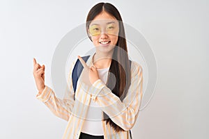 Young chinese student woman wearing glasses and backpack over isolated white background smiling and looking at the camera pointing
