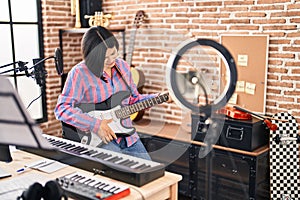 Young chinese woman artist having online electrical guitar class at music studio