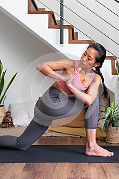 Young Chinese woman doing low lunge twist yoga pose at home. Parivrtta anjaneyasana home yoga practice. Vertical image.