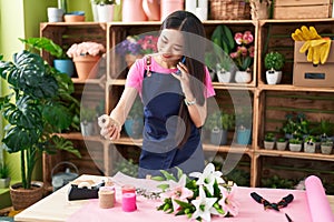 Young chinese woman florist talking on smartphone holding gift lace at flower shop