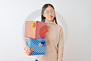 Young chinese woman holding birthday gifts over isolated white background smiling looking to the side and staring away thinking