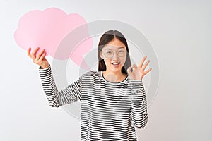 Young chinese woman holding cloud speech bubble over isolated white background doing ok sign with fingers, excellent symbol