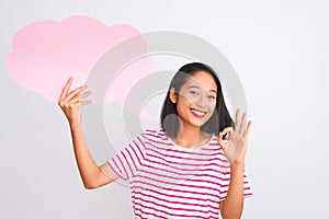 Young chinese woman holding cloud speech bubble standing over isolated white background doing ok sign with fingers, excellent