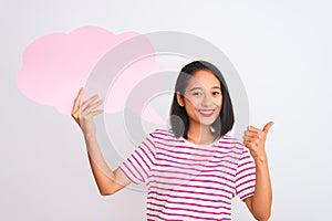 Young chinese woman holding cloud speech bubble standing over isolated white background happy with big smile doing ok sign, thumb