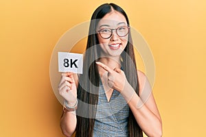 Young chinese woman holding 8k resolution technology paper smiling happy pointing with hand and finger photo