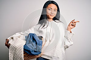 Young chinese woman holding wicker basket with clothes over isolated white background very happy pointing with hand and finger to