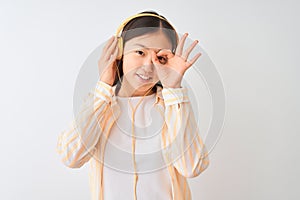 Young chinese woman listening to music using headphones over isolated white background with happy face smiling doing ok sign with