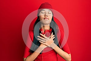 Young chinese woman listening to music using headphones smiling with hands on chest with closed eyes and grateful gesture on face
