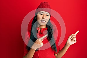 Young chinese woman listening to music using headphones smiling and looking at the camera pointing with two hands and fingers to