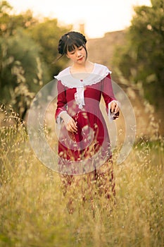 Young Chinese woman in red retro style dress, walking and traveling in a meadow field, France, Europe