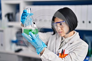 Young chinese woman scientist holding measuring liquid at laboratory