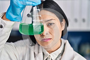 Young chinese woman scientist holding test tube over eye at laboratory