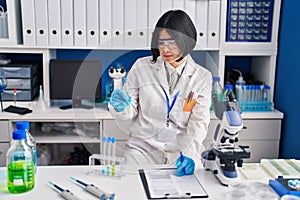 Young chinese woman scientist holding test tube write on report document at laboratory