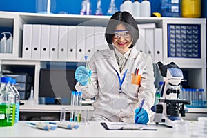 Young chinese woman scientist holding test tube write on report document at laboratory