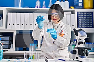 Young chinese woman scientist pouring liquid on test tube at laboratory