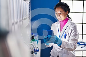 Young chinese woman scientist smiling confident using touchpad at laboratory