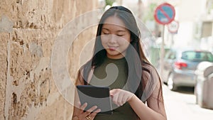 Young chinese woman smiling confident using touchpad at street