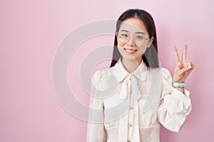 Young chinese woman standing over pink background showing and pointing up with fingers number two while smiling confident and