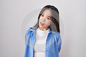 Young chinese woman standing over white background in shock face, looking skeptical and sarcastic, surprised with open mouth