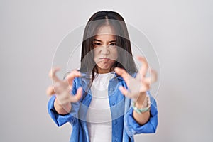 Young chinese woman standing over white background shouting frustrated with rage, hands trying to strangle, yelling mad