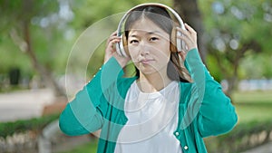 Young chinese woman standing with serious expression listening to music at park