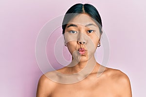 Young chinese woman standing topless showing skin puffing cheeks with funny face