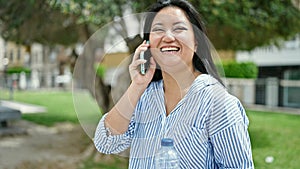 Young chinese woman talking on the smartphone holding bottle of water at park