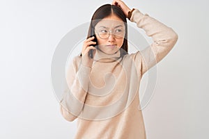 Young chinese woman talking on the smartphone over isolated white background confuse and wondering about question