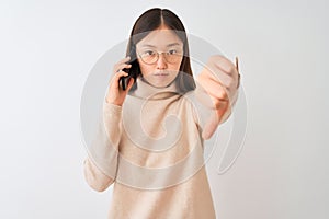 Young chinese woman talking on the smartphone over isolated white background looking unhappy and angry showing rejection and