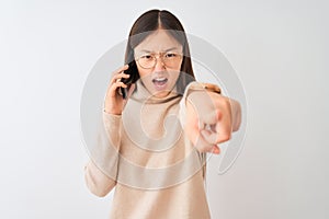 Young chinese woman talking on the smartphone over isolated white background pointing displeased and frustrated to the camera,