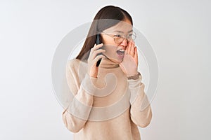 Young chinese woman talking on the smartphone over isolated white background shouting and screaming loud to side with hand on