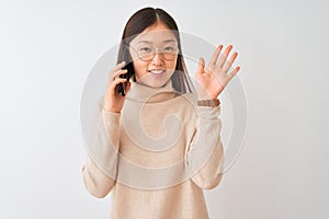 Young chinese woman talking on the smartphone over isolated white background Waiving saying hello happy and smiling, friendly
