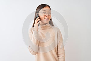 Young chinese woman talking on the smartphone over  white background looking away to side with smile on face, natural
