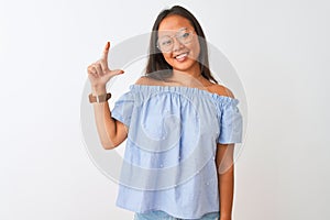 Young chinese woman wearing blue t-shirt and glasses over isolated white background smiling and confident gesturing with hand