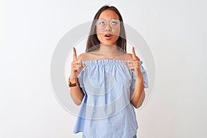 Young chinese woman wearing blue t-shirt and glasses over  white background amazed and surprised looking up and pointing