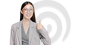 Young chinese woman wearing business clothes smiling happy and positive, thumb up doing excellent and approval sign